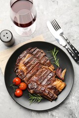 Delicious grilled beef steak with rosemary, onion and tomatoes served on grey textured table, flat lay