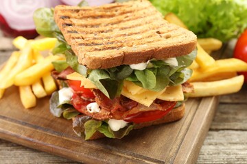 Tasty sandwich served with french fries on wooden table, closeup