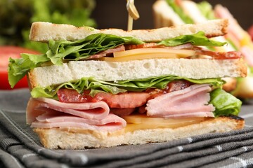 Tasty sandwiches with ham, bacon, cheese and vegetables on table, closeup
