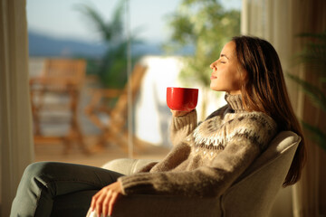 Woman in winter at home drinking coffee from red cup