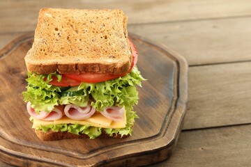 Tasty sandwich with ham, cheese and vegetables on wooden table, closeup. Space for text