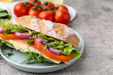 Obraz premium Delicious ciabatta sandwich with prosciutto, cheese and vegetables on light grey table, closeup. Space for text