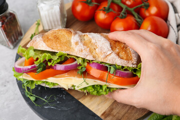 Woman taking delicious ciabatta sandwich at light table, closeup