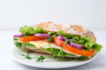 Delicious ciabatta sandwich with prosciutto, cheese and vegetables on white tiled table, closeup