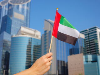 female hanwoman holding tiny flag of UAE against Abu Dhabi skyline, Promenade in Abu Dhabi. United Arab Emirates, Middle East. Immigration, student education and Arab emirated holding tiny flag of UAE