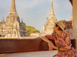 Young female tourist in dress exploring historic park of Ayutthaya, Thailand. Surrounded by ancient temples and statues, she enjoys peaceful atmosphere and rich cultural heritage.