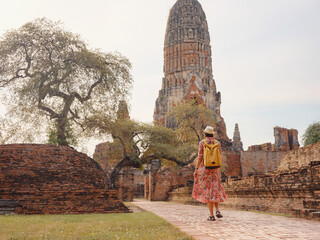 Young female tourist in dress exploring historic park of Ayutthaya, Thailand. Surrounded by ancient temples and statues, she enjoys peaceful atmosphere and rich cultural heritage.