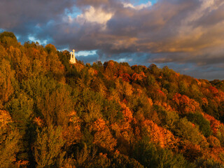 Aerial view of the Three Crosses Monument stands silhouetted against a dramatic sky, amidst a vibrant tapestry of autumn foliage, Vilnius, Lithuania.
