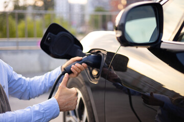 A person plugs an electric vehicle into a charger, giving a thumbs up, symbolizing approval and satisfaction with the charging process.