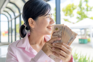 Confident Asian woman holding Thai baht banknotes, Money, Cash, Wealth, symbolizing financial stability, income growth, and personal success