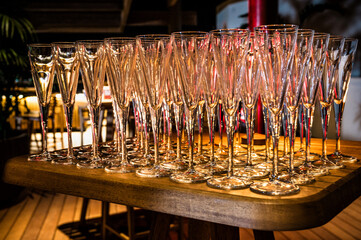Close-up of many empty champagne glasses arranged neatly across wooden table, illuminated by warm light, creating elegant atmosphere suitable for celebration preparation or event setup.