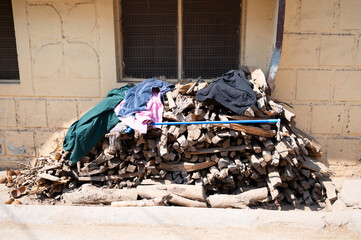 Chopped tree logs pill in front of a house, broom and cleaned clothes, lumber wood used for cooking and heating in India