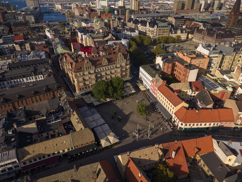 Aerial view of Lilla Torg's cobblestone square, framed by historic buildings with terracotta roofs and shadowed alleys, casting a warm glow across the city, Malmo, Sweden.