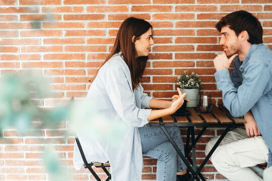 Young man and woman sitting face to face at a small table chatting and laughing like close friends or couple, sharing secrets, gossip and stories about love, school, work and everyday life conversatio