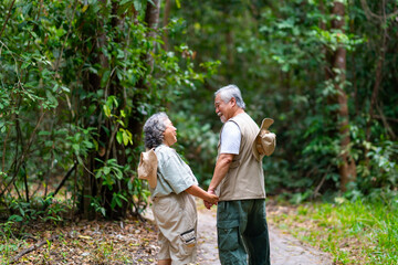 Happy Asian senior couple travel nature hiking and camping at tropical forest on summer vacation. Healthy elderly retired husband and wife enjoy outdoor active lifestyle walking forest trail together.