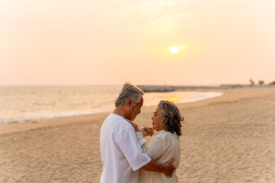 Happy Asian family senior couple dancing on the beach at sunset. Healthy elderly husband and wife enjoy outdoor lifestyle travel nature at the sea in summer. Old people mental health wellness - Powered by Adobe