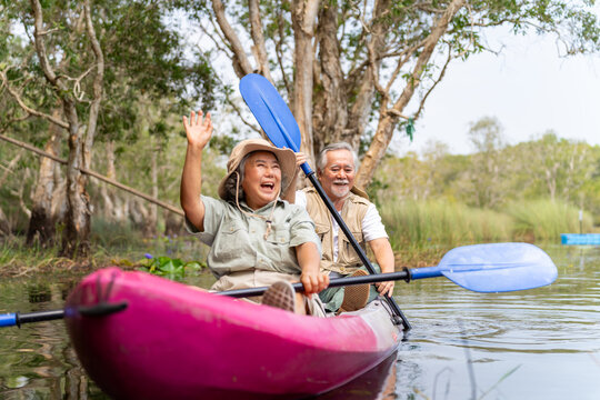 Happy Asian senior couple kayaking in the river on summer holiday vacation. Healthy retired elderly people enjoy and fun outdoor active lifestyle travel nature, sport and rowing a boat in the lake. - Powered by Adobe