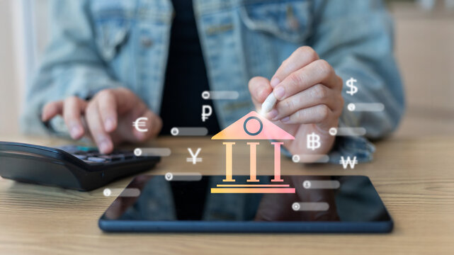 A person using a digital pen and calculator with a holographic bank icon, representing digital banking, fintech innovation, and a global online currency exchange system.