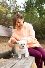 Senior Woman petting maltese dog sitting on park bench