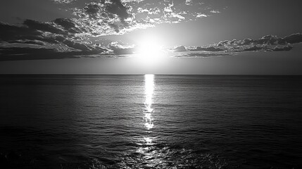 Black and white sunset over a calm sea.  Vast expanse of water meets a brilliant sun