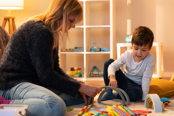 Babysitter and child playing with colorful wooden building blocks on floor