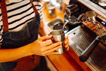 An experienced barista prepares freshly brewed coffee in a cozy cafe. A young woman froths and pours milk into an espresso. Small business concept, beverages.