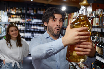 A man is holding a large bottle of tequila in a liquor store