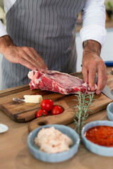 Chef's hands trimming a raw beef steak on a wooden cutting board with fresh ingredients