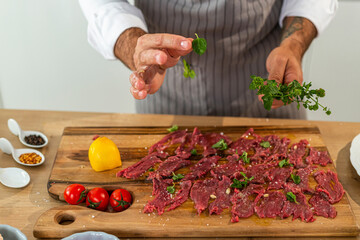 Chef adding fresh herbs to carpaccio on wooden cutting board