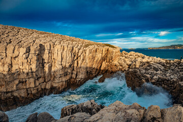 Jagged sea cliffs and foamy waves create a powerful coastal landscape under a deep blue sky.