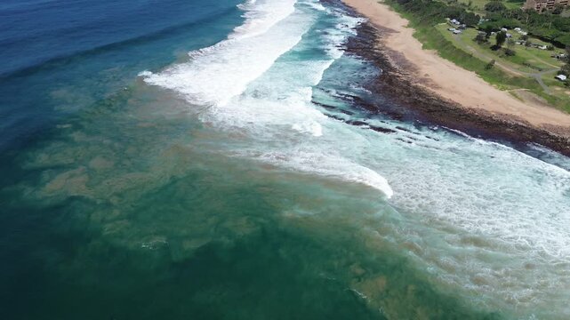Camera panning up from the deep blue ocean over white waves, looking down the South Coast of KwaZulu-Natal to the coastal town of Scottburgh, Aerial 4K video.