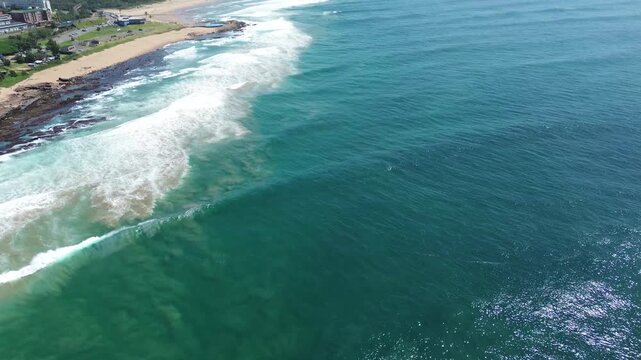 Camera panning up from the deep blue ocean over white waves, looking down the South Coast of KwaZulu-Natal to the coastal town of Scottburgh, Aerial 4K video.