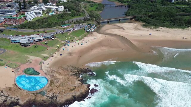 Camera panning up of the beach and tidal pool towards the rolling green hills of the South Coast of KwaZulu-Natal the coastal town of Scottburgh, Aerial 4K video.