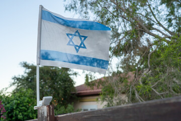 An Israeli flag waves in the breeze, symbolizing national pride, unity, and relief as people celebrate the liberation and safe return of hostages, surrounded by nature and home. 