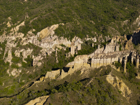 Aerial view of rugged, sun-drenched rock formations rise amidst the verdant hills, creating a striking contrast of earth tones and lush greenery, La Playa, Santander, Colombia.