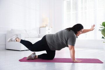 Fototapeta premium Overweight woman in sportswear stretching on yoga mat at home