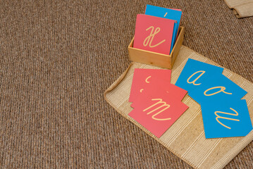 Montessori written sensory materials. Pink and blue wooden letter cards on a learning mat. Develops muscle memory, understanding of shape and hand movements in elementary school.