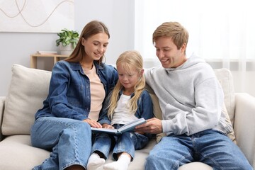 Little girl looking through photo album with her parents on sofa at home
