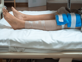 Obraz premium Patient lying in hospital bed with bandaged knee and cold pack after ACL and meniscus surgery. Concept of post-surgery recovery, orthopedic injury, rehabilitation, physical therapy, and medical care.