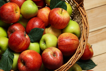 Fresh apples in wicker basket and green leaves on wooden table, above view