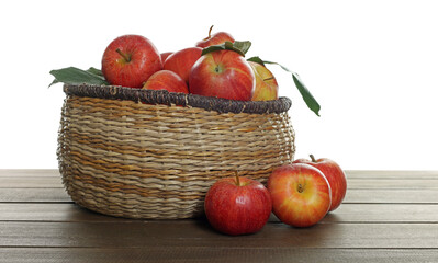 Fresh apples in wicker basket and green leaves on wooden table against white background