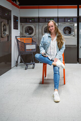 Woman sitting on orange chair in self service laundry with washing machines in background