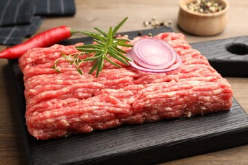 Raw minced meat with rosemary, thyme and spices on wooden table, closeup