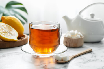 Aromatic black tea in glass cup, sugar and lemons on white marble table, closeup