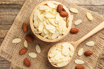 Fresh almond flakes and whole nuts on wooden table, flat lay
