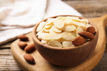 Fresh almond flakes and whole nuts in bowl on wooden table, closeup