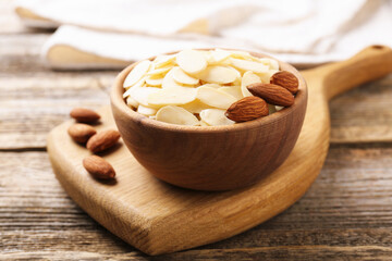 Fresh almond flakes and whole nuts in bowl on wooden table, closeup