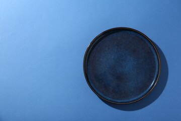 Stylish ceramic plate on blue background, top view. Space for text