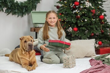 Girl holding Christmas gift while sitting with dog near tree