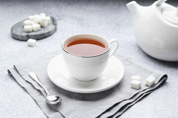 Aromatic black tea in cup, sugar, teapot and spoon on light grey table, closeup